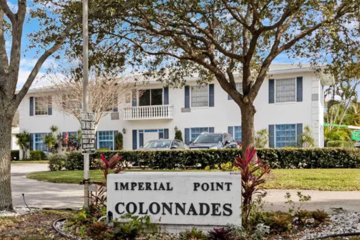 A scenic view of a well-maintained neighborhood street in Imperial Point Colonnades, Fort Lauderdale, with trees, greenery, and residential homes.